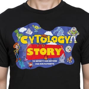 Könnte beinhalten: Schwarzes T-Shirt mit einem farbenfrohen Grafikdesign. Das Design zeigt die Worte "CYTOLOGY STORY" mit Cartoon-Figuren und wissenschaftlichen Bildern. Das T-Shirt enthält auch den Text "TO INFINITY AND BEYOND FOR OUR PATIENTS!"