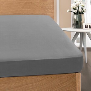 May include: A fitted gray bed sheet on a wooden bed frame. The sheet is a solid color and appears to be made of a soft fabric. The bed frame is made of light-colored wood. The overall theme is bedroom decor.