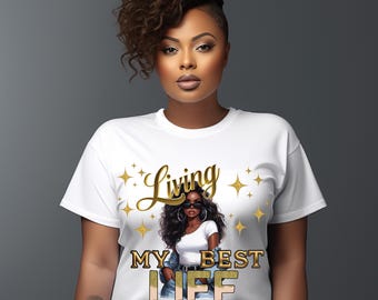 May include: White t-shirt with a graphic of a woman wearing sunglasses and the text "Living My Best Life" in gold script and leopard print. The design includes gold stars. The shirt is a casual wear item.