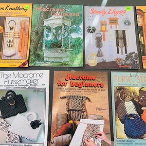May include: Seven instructional craft books featuring macrame projects. Titles include Kitchen Knotter, Macrame Unlimited, Simply Elegant, Purse Magic, The Macrame Pursemaker, Macrame for Beginners, and Purse Strings, displaying various bags and decor.