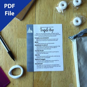 May include: A flat lay featuring a gray drawstring bag, a printed card with text, mints in clear packaging, a pen, a comb, and a white hair tie. The card reads "Temple Bag" and lists items needed for a baptism trip.