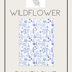 May include: A watercolor floral pattern in shades of blue and green on a white background. The design features small flowers and leaves. The text "WILDFLOWER" and "DAINTY BLUE" are displayed above and below the pattern, respectively. The brand name "joy by j&j" is at the top.