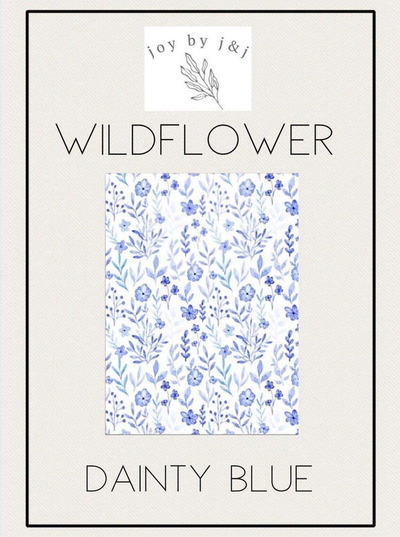 May include: A watercolor floral pattern in shades of blue and green on a white background. The design features small flowers and leaves. The text "WILDFLOWER" and "DAINTY BLUE" are displayed above and below the pattern, respectively. The brand name "joy by j&j" is at the top.