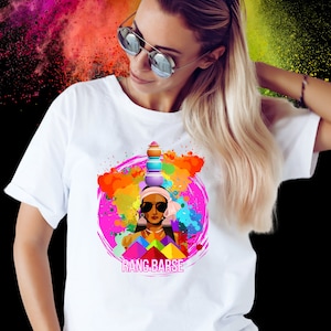 May include: White t-shirt featuring a colourful graphic design of a woman wearing sunglasses and a traditional Indian headpiece. The graphic also includes a circle of colourful paint splatters and the text "RANG-BARSE".