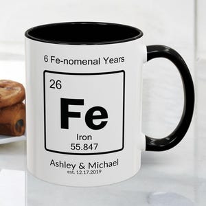 May include: White ceramic mug with a black interior and handle. The mug features the periodic symbol for iron, "Fe", with the text "6 Fe-nomenal Years" and the names "Ashley & Michael" with the date "est. 12.17.2019".