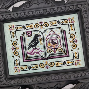 May include: Cross-stitch artwork in a black frame. The design features a raven holding a key, and a caged bird, set against a light blue background. The artwork is framed with decorative borders in black, gold, and purple.