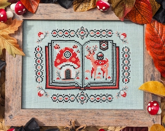 May include: A framed cross-stitch design featuring a book with a mushroom house and a deer on the cover. The book is surrounded by a red and black border. The frame is made of wood and has a light brown finish.