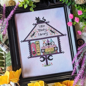 May include: A black framed cross-stitch design of a witch's library with a black cat on top. The library is filled with books and potions. The text reads "Little Witchy Library".