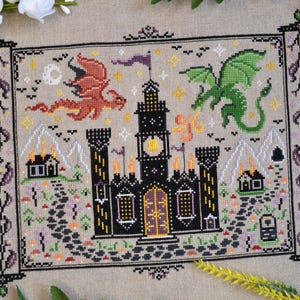 May include: Cross-stitch design featuring a black castle with a yellow clock tower, flanked by two dragons, one red and one green. The scene includes mountains, houses, and a path, all framed by a decorative border. The color palette includes black, yellow, green, and purple.
