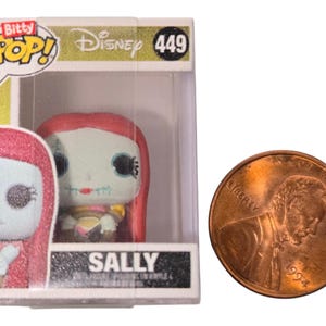 May include: A Bitty Pop! Disney Sally figure in a clear plastic display case. The figure has a light blue face, red hair, and a stitched mouth. A penny is next to the figure for size comparison. The box reads "SALLY".