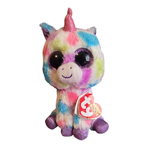 May include: A colorful plush unicorn toy with a pink horn and large glittery eyes. The unicorn is sitting with its legs crossed and has a red and white "Ty" tag attached to its side.
