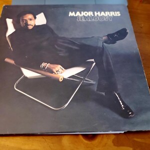 May include: Album cover for Major Harris' "Jealousy." The cover features a man in a black suit reclining in a chair. The album title and artist's name are in white text at the top. The background is a gradient of dark blue.