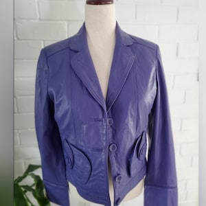 May include: A purple leather jacket with a button closure and decorative pockets. The jacket has a cropped length and long sleeves.