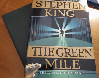 Puede incluir: Una portada de libro de bolsillo con un fondo verde y el título "The Green Mile" en letras doradas grandes. El autor, Stephen King, está impreso en letras negras grandes sobre el título. La portada del libro presenta a un hombre caminando por un pasillo con una luz brillante al final.