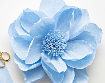 May include: A large, light blue paper flower with a ruffled texture. The flower has a centre made of smaller, ruffled paper pieces.
