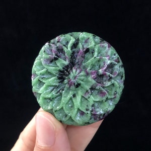 Peut inclure: Un pendentif en pierre sculptée en forme de fleur, de couleur verte et rose, avec un motif floral détaillé. La pierre a un aspect marbré avec des nuances de noir, de vert et de rose.