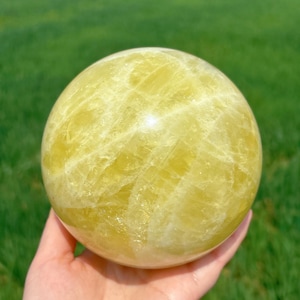 May include: A large, yellow citrine sphere with a smooth, polished surface. The sphere has a translucent appearance and shows intricate patterns of light and dark yellow.
