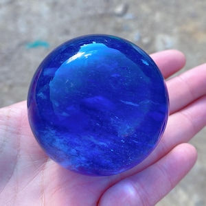 Op de afbeelding: Een grote, ronde, blauwe kristallen bol met witte swirls en strepen. De bol is glad en gepolijst.