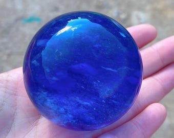 Puede incluir: Una gran bola de cristal redonda y azul con remolinos y rayas blancas. La bola es lisa y pulida.