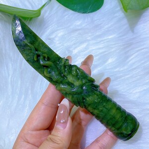 May include: A green jade knife with a dragon carving on the handle. The blade is smooth and polished, while the handle features detailed dragon scales. The jade has varying shades of green.