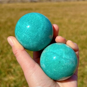 Puede incluir: Dos esferas de amazonita verde pulidas y lisas. Las esferas tienen aproximadamente el tama&ntilde;o de una pelota de golf y son de color verde claro con vetas blancas.