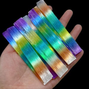 May include: A collection of iridescent rainbow coloured glass rods. The rods are stacked on top of each other and have a shimmery finish.