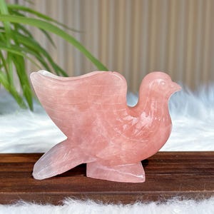 May include: A pink rose quartz dove figurine. The dove is carved with detailed feathers and has a delicate, feminine appearance.