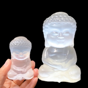 May include: Two white, opaque, glass Buddha statues in a seated meditation pose. The larger statue is about 10 inches tall and the smaller statue is about 5 inches tall.