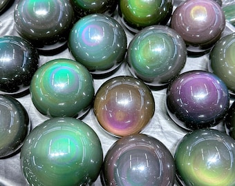 May include: A collection of iridescent obsidian spheres in various shades of green, purple, and black. The spheres are smooth and reflective, creating a mesmerizing optical effect.