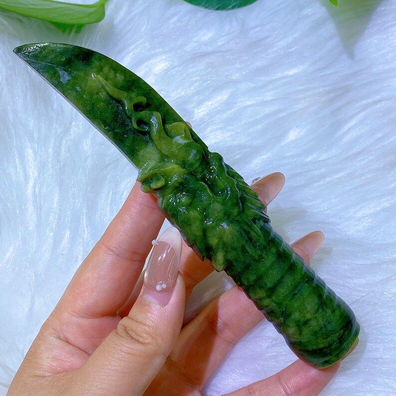 May include: A carved green jade knife with a dragon design. The blade is flat and the handle is textured. The knife is approximately 7 inches long.