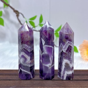 May include: Three amethyst crystal points with a white and purple swirl pattern. The points are arranged in a row on a wooden surface.
