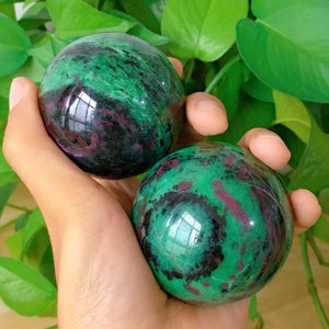 Könnte beinhalten: Zwei grüne, schwarze und rosafarbene Edelsteinkugeln. Die Kugeln sind glatt und poliert.