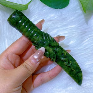 May include: A hand-carved, green jade knife with intricate dragon detailing. The jade is a deep, rich green color, and the knife has a pointed blade. The handle is textured with a ridged pattern. The dragon is carved on the handle and blade.