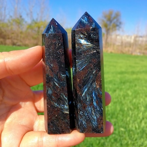 Op de afbeelding: Twee donkerblauwe en bruine kristallen punten met een glinsterende, iriserende afwerking. De punten zijn ongeveer 10 cm lang en hebben een puntige punt.