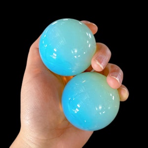 May include: Two smooth, round, iridescent spheres in shades of blue and green. The spheres are made of polished glass or crystal and have a subtle, shimmering effect.