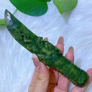 May include: A green jade knife with a carved dragon design on the handle. The blade is sharp and pointed. The knife is a vibrant shade of green with darker green marbling throughout. The handle has a textured, ridged design.