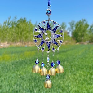 May include: A silver and blue sun and moon wind chime with a blue evil eye charm hanging from each bell. The chime is decorated with a silver and blue sun and moon design.