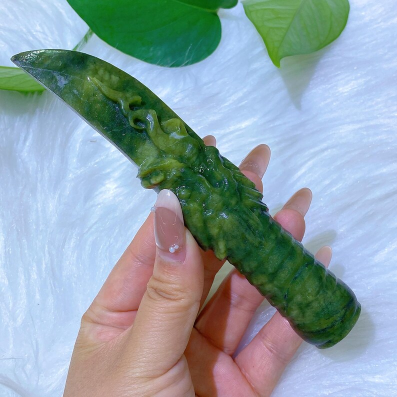 May include: A jade green decorative knife with a dragon carving on the handle. The blade is a darker shade of green, and the handle has a textured, organic appearance. The knife is displayed against a soft, white background.