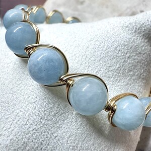 May include: A bracelet made with light blue gemstone beads wrapped in gold wire.
