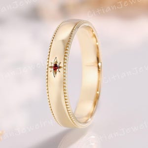 Op de afbeelding: Een goudkleurige ring met een stervormige rode edelsteen. De ring heeft een kralenrand en een glad, gepolijst oppervlak. De ring is maat 17.