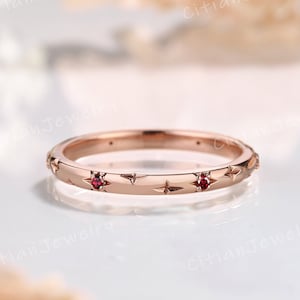 May include: A delicate rose gold band ring with a row of small red gemstones set in a star-shaped design.