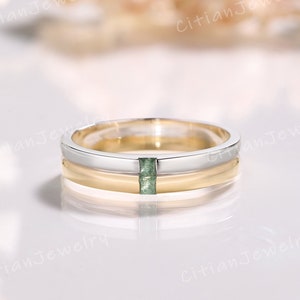 Puede incluir: Una banda de boda de dos tonos, oro y plata, con una pequeña piedra preciosa verde engastada en el centro.