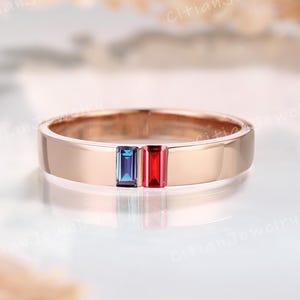 May include: Rose gold ring with a flat band, featuring a blue and red rectangular gemstone design. The ring has a polished finish and is set against a soft, blurred background. The text "Citian Jewelry" is visible.