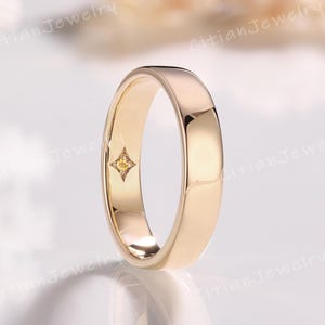 May include: A polished gold band ring with a smooth, rounded exterior surface. The interior of the band features a small, four-pointed star-shaped setting containing a single, tiny, round-cut yellow gemstone centered within the metal band.