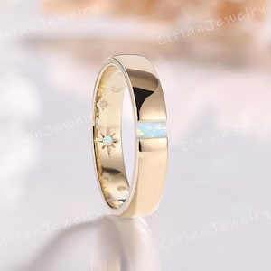 Puede incluir: Un anillo de banda de oro con un acabado pulido liso y una incrustación de ópalo rectangular única. El interior de la banda está grabado con motivos celestiales, incluyendo una pequeña estrella con un diminuto centro de ópalo y lunas.