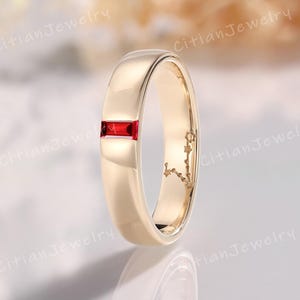 May include: A gold-colored ring with a rectangular, bright red gemstone set in the center. The ring has a smooth, polished surface and a simple, elegant design. The ring is a classic piece of jewelry.