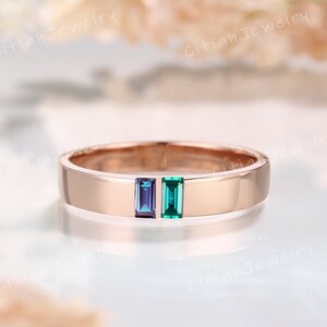May include: A rose gold band ring featuring two baguette-cut gemstones set side-by-side in the centre. One gemstone is a deep purple-blue, and the other is a vibrant green. The metal has a smooth, polished finish with the text CitianJewelry.