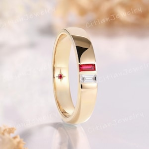 May include: A gold band ring featuring a rectangular baguette-cut red ruby and a rectangular baguette-cut white diamond set vertically. The inner band displays a small star-shaped engraving with a tiny embedded red gemstone at its center.