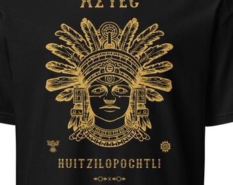 May include: A black short-sleeve t-shirt featuring a gold-colored graphic print of an Aztec figure wearing an elaborate feathered headdress. The text AZTEC is printed above the figure, and HUITZILOPOCHTLI is printed below, with small symbols.