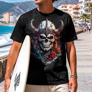 Puede incluir: Camiseta negra con un diseño detallado de calavera con casco vikingo, cuernos y detalles florales. La calavera tiene ojos rojos brillantes, rodeada de rosas coloridas y flores azules. La persona lleva la camiseta y sostiene una tabla de surf.